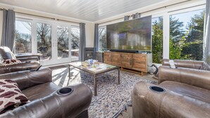 A spacious living room with leather sofas, a coffee table, and a large flat-screen TV.