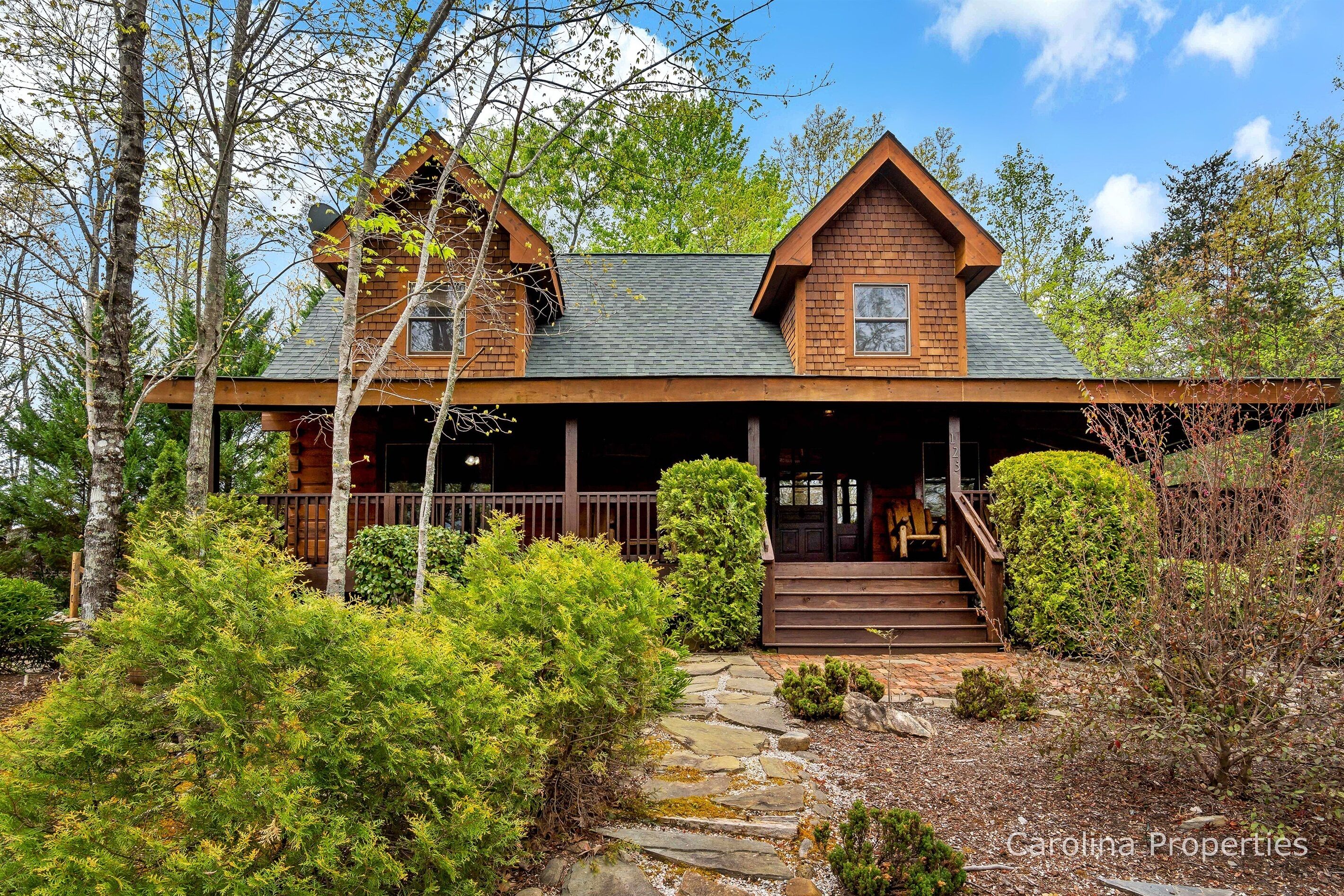 A rustic cabin with a stone pathway leading to a wooden porch, surrounded by dense greenery.