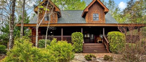 A rustic cabin with a stone pathway leading to a wooden porch, surrounded by dense greenery.