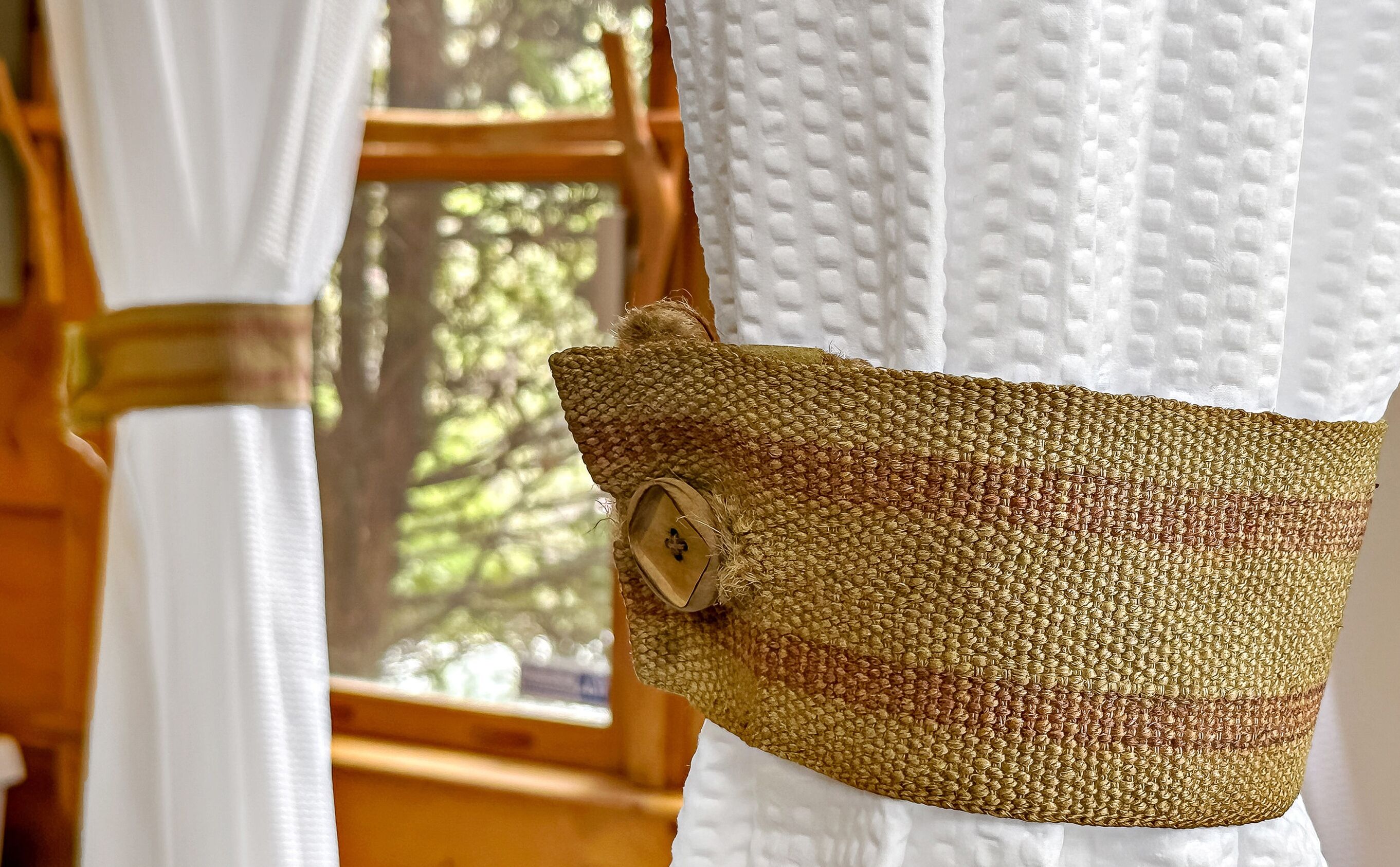 A woven bag hanging on a white curtain.