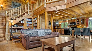 Ein gemütliches Blockhaus-Interieur mit einer Holztreppe, einem Wohnzimmer mit Sofa und Couchtisch, einer Küchenzeile und einem Essbereich.
