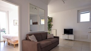 A modern living room with a brown sofa, a TV on a white cabinet, and a large mirror on the wall.