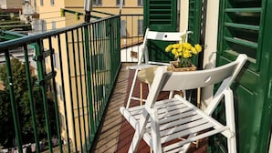 A balcony with a tiled floor, green shutters, and white chairs.