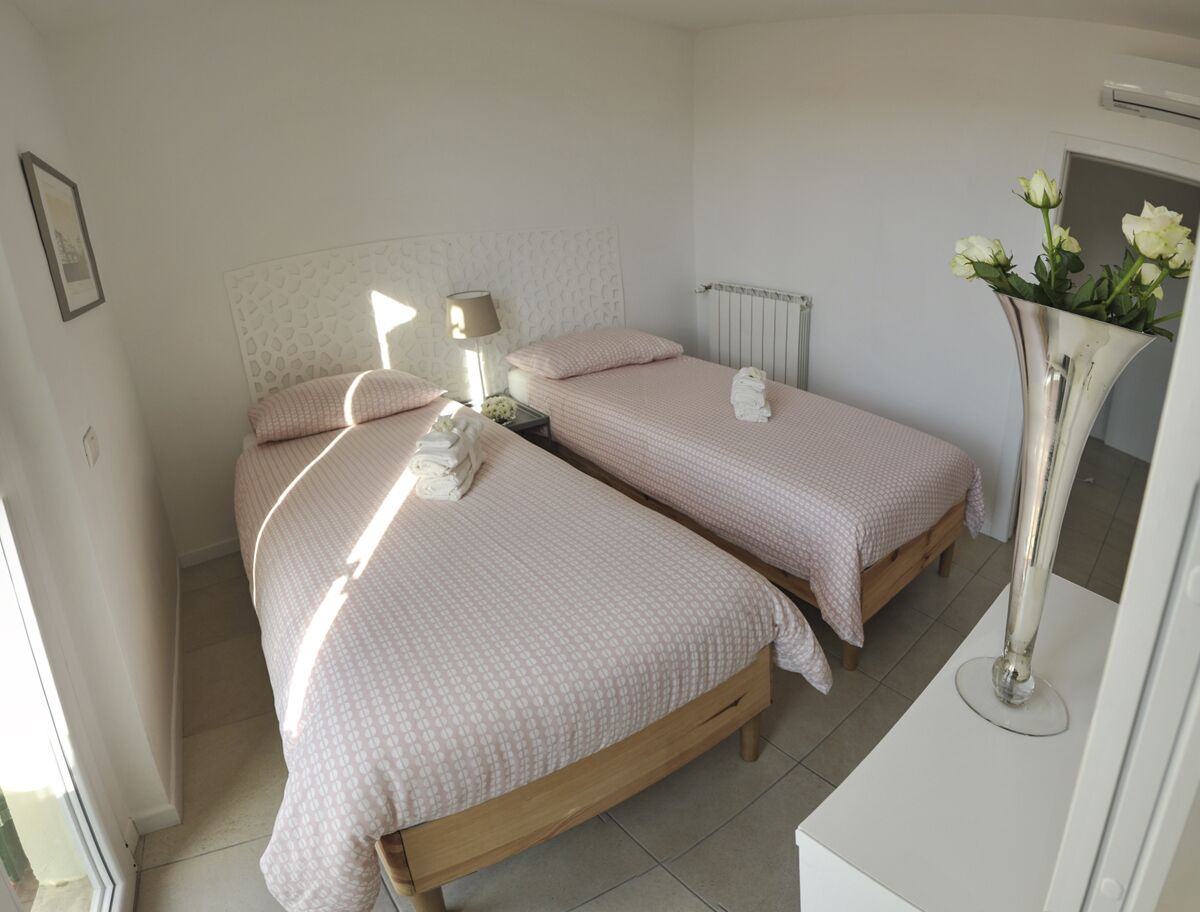 Ein Zimmer mit zwei Betten, einem Nachttisch mit Lampe, einem Heizkörper und einer Vase mit Blumen.