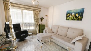 A living room with a beige sofa, a glass coffee table, a black armchair, a green side table, and a painting of flowers on the wall. - A93 SENIA ESC C  2º I (Calpe)