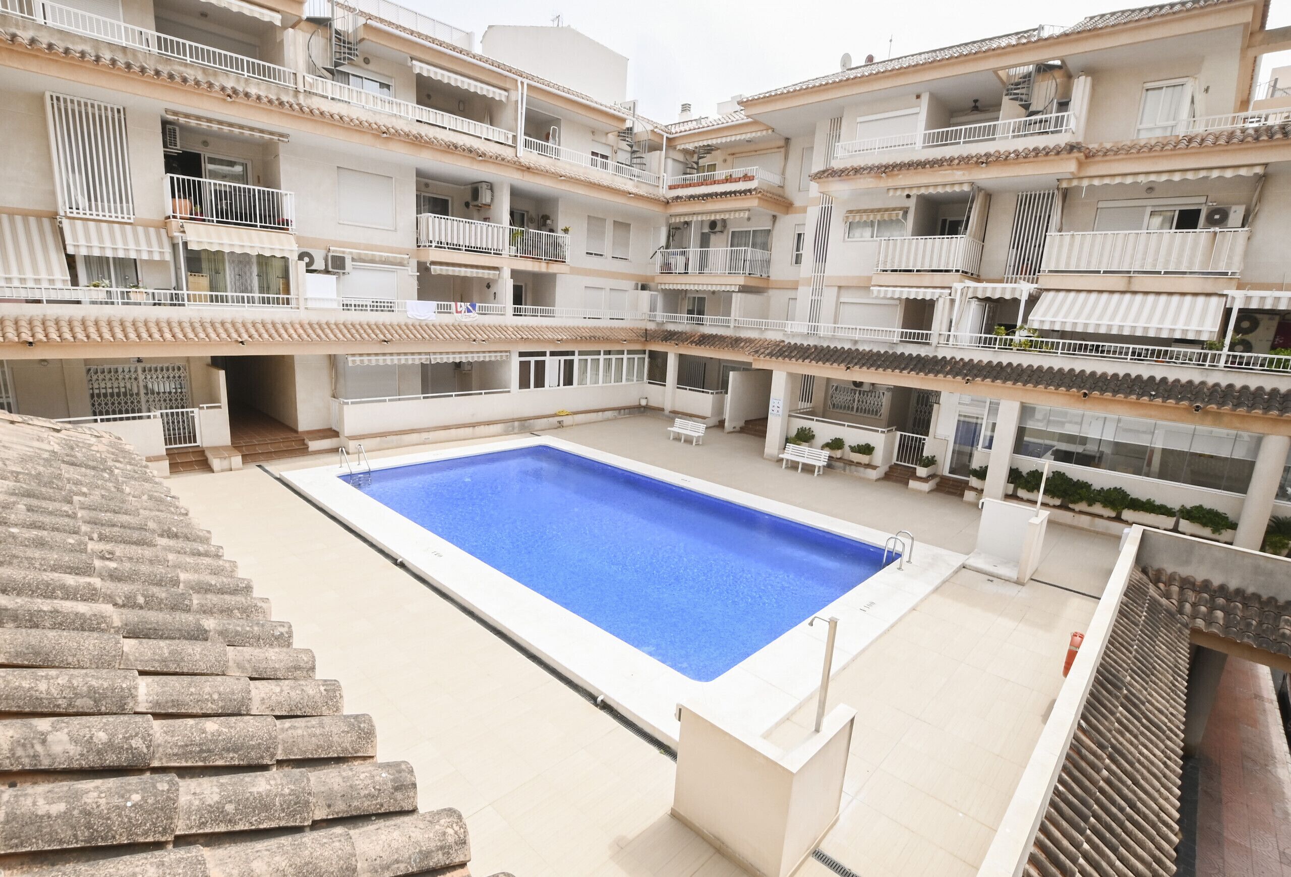 Un edificio residencial de varios pisos con piscina central, balcones y zonas de estar al aire libre.