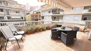 A rooftop terrace with a table and chairs, surrounded by potted plants, and overlooking a residential area. - A93 SENIA ESC C  2º I (Calpe)