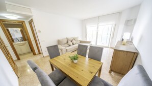 A dining area with a wooden table and grey upholstered chairs, a small potted plant on the table, and a sofa in the background.