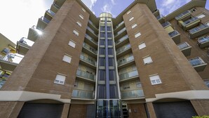 A multi-story residential building with a central glass elevator shaft, balconies on each floor, and garage doors at the ground level.