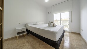 A bedroom with a bed, a nightstand, a window, and a view of the outside.