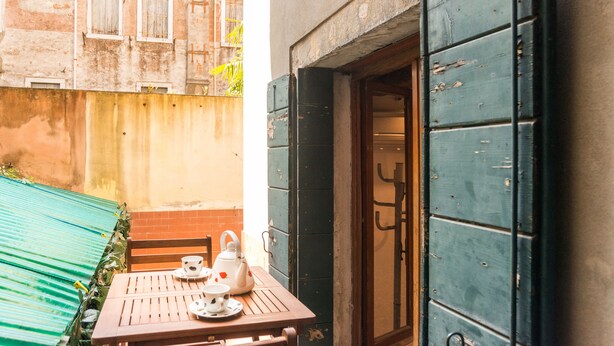 Una pequeña mesa al aire libre con un calentador de agua y tazas, un banco de madera y un toldo verde.