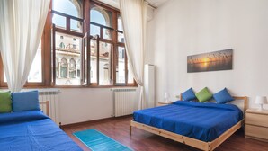 Un dormitorio con dos camas, vista de un edificio a través de una ventana y un cuadro en la pared.