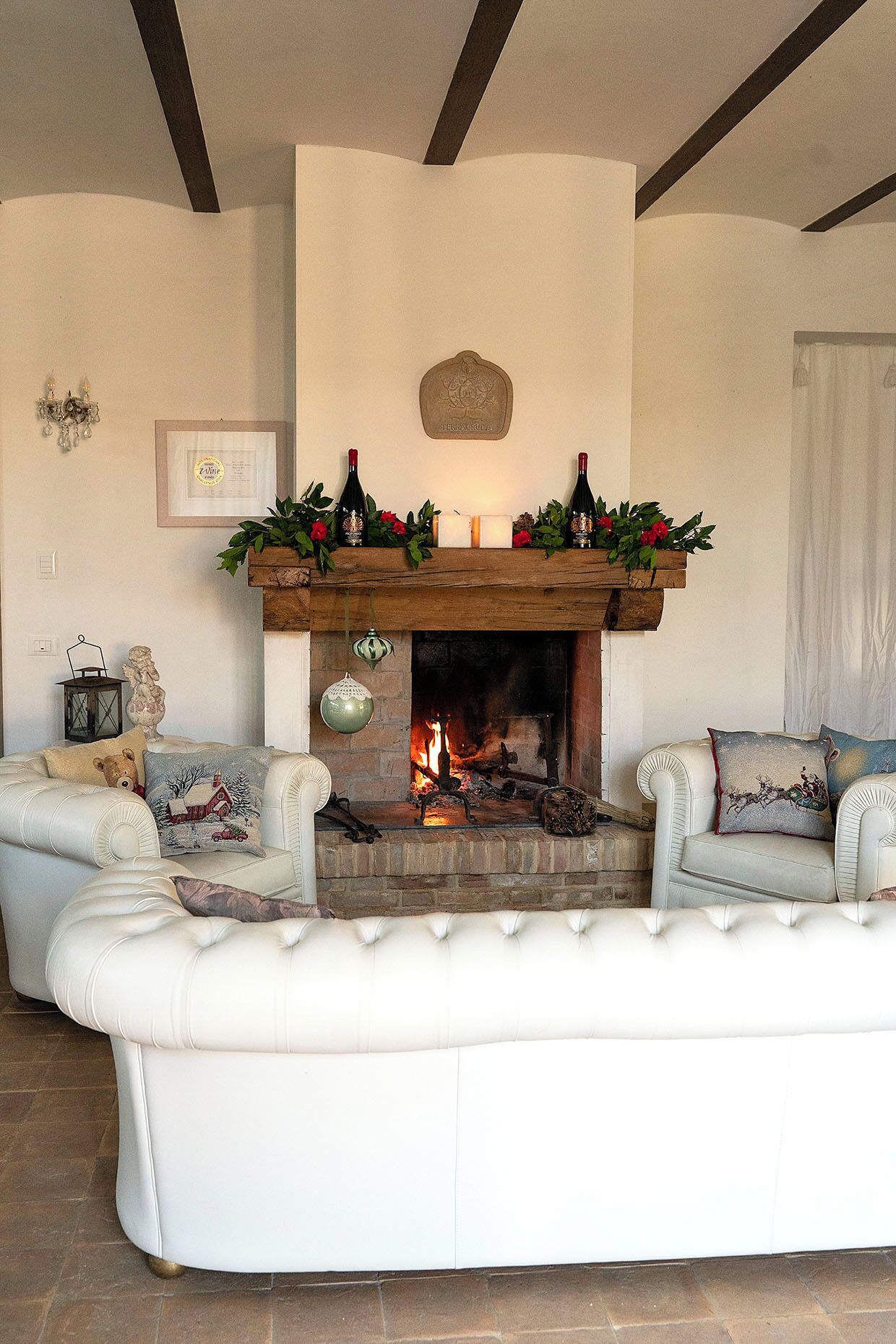 A cozy living room with a fireplace, white leather sofas, and a mantel decorated with flowers and candles.