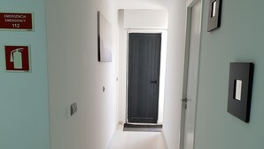 A narrow hallway with a dark door at the end, white walls, and a fire extinguisher on the left. - Mikaela Guest House (Odivelas)
