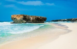 Ein Strand mit klarem türkisblauem Wasser, einer großen Felsformation und einem Sandufer.