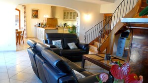 A living room with a black leather sofa, a wooden coffee table, and a staircase leading to a kitchen area.