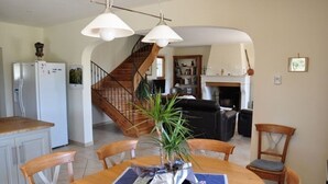 A dining area with a wooden table, chairs, and a potted plant. A staircase leads to another room.