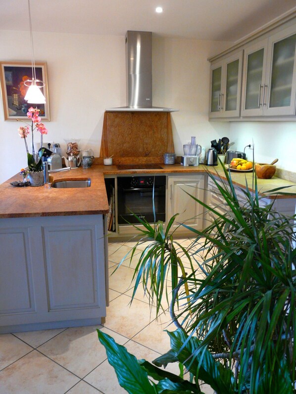 A kitchen with a central island, a stainless steel range hood, and a variety of appliances and utensils on the countertops.