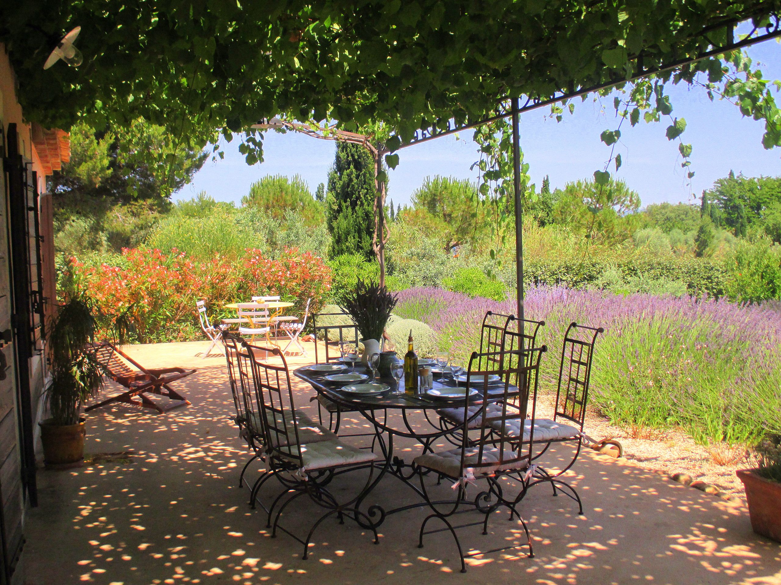 An outdoor patio with a table set for dining, surrounded by chairs, and a pergola overhead.