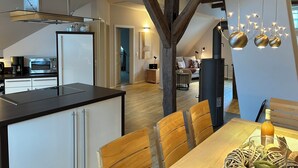 A modern kitchen with a central island, a dining area with wooden chairs, and a visible staircase leading to an upper level. - Half-timbered love Ornes 3 (Olsberg)