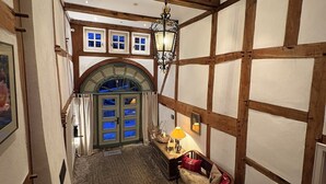 A room with exposed wooden beams, a chandelier, a fireplace, and a view of a blue-lit door. - Half-timbered love Ornes 3 (Olsberg)