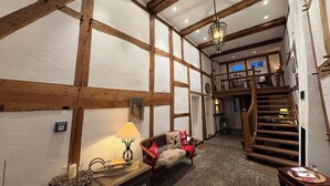 A traditional inn with exposed wooden beams, a cozy sitting area with a lamp, and a staircase leading to an upper level. - Half-timbered love Ornes 3 (Olsberg)