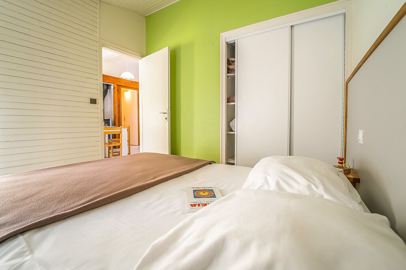 A bedroom with a bed, a green wall, a white wardrobe, and a wooden door.