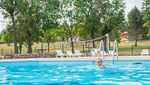 Piscina con una persona nadando, rodeada de árboles y una valla.