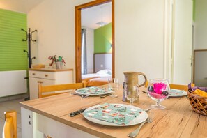 Uma mesa de jantar posta com pratos, talheres, jarra e copos, com vista para um quarto ao fundo.
