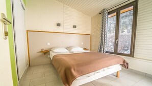 Un dormitorio con cama, mesitas de noche, una ventana con cortinas y vistas a árboles.