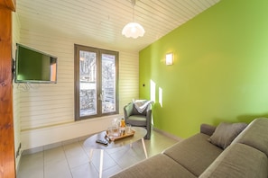 Uma sala de estar com parede verde, um sofá, uma mesa de centro e uma TV fixada na parede.