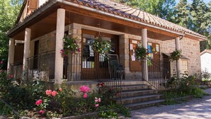 Un edificio de piedra con tejado de tejas, un porche de madera y un jardín con flores rosadas.