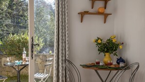 An outdoor dining area with a table set for two, a vase of yellow flowers, and a view of a stone wall and greenery.