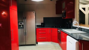A modern kitchen with red cabinets, a stainless steel refrigerator, a black countertop, and a white sink.