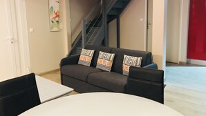 A modern living room with a grey sofa, patterned cushions, a white table, and a staircase.