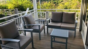 A balcony with two grey cushioned chairs and a small table, overlooking a lush green landscape.