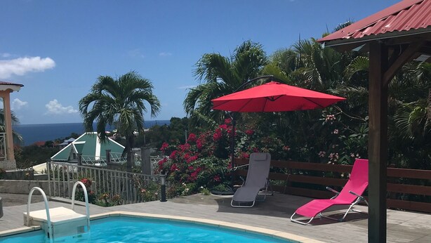 A swimming pool with a slide, a red umbrella, and a view of the ocean.