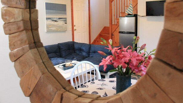 Ein Wohnzimmer mit einem dunkelblauen Sofa, einem weißen Sessel, einem Tisch mit einer Tablettauswahl und einer Vase mit rosa Blumen.