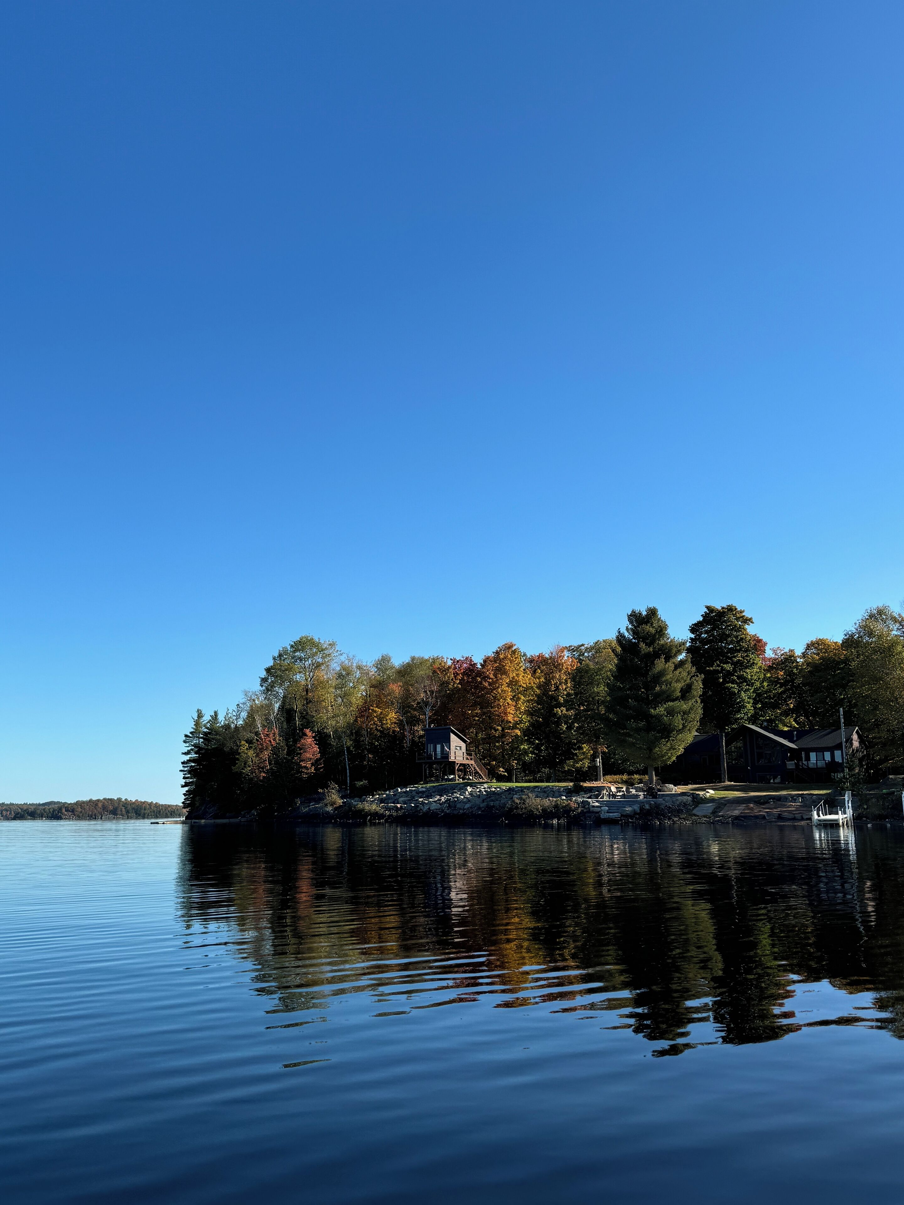 A calm lake with a wooden dock and a house surrounded by trees.