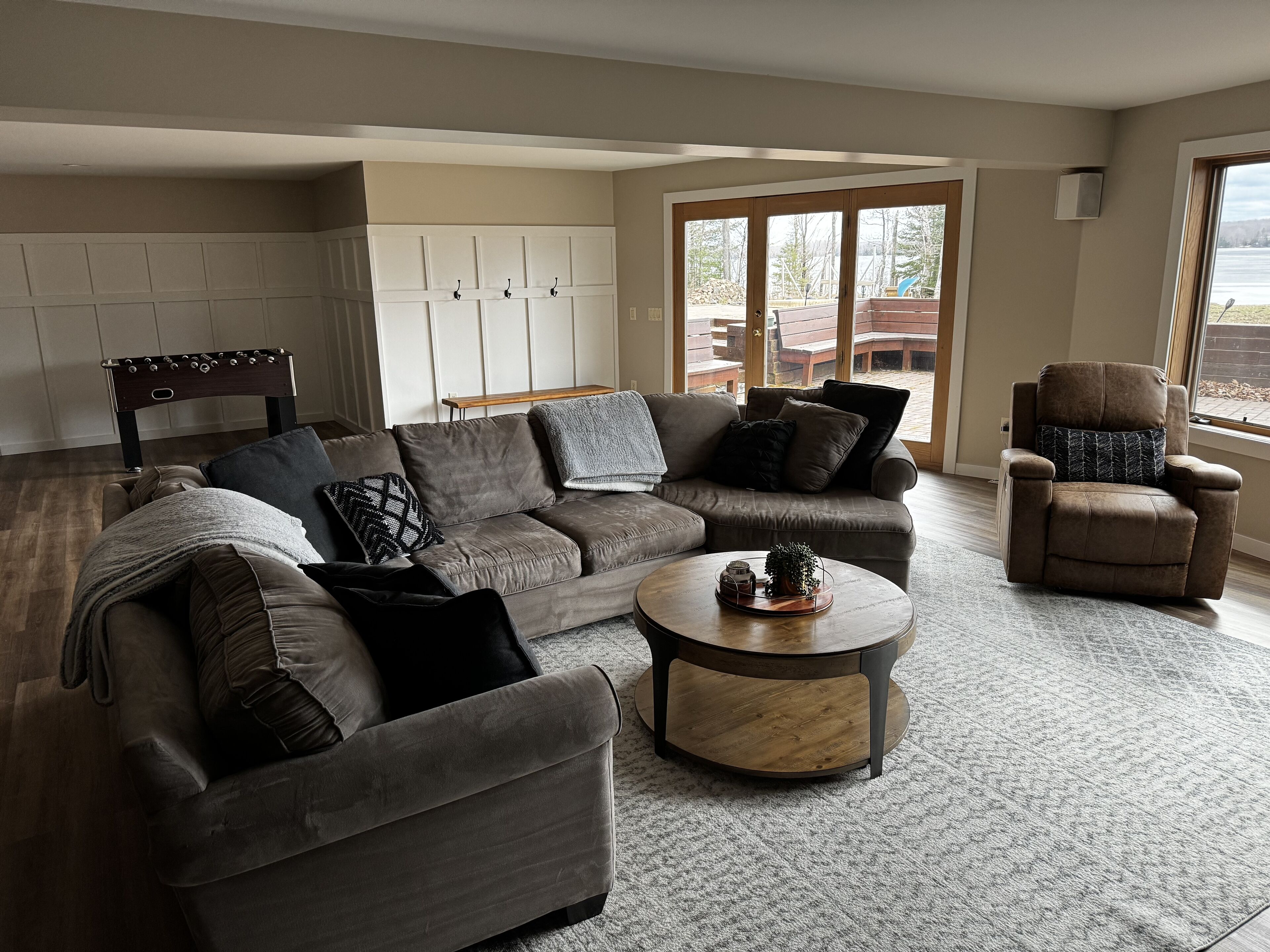 Una sala moderna con un sofá seccional gris, una mesa de centro redonda y un sillón reclinable. Una ventana grande ofrece vistas del exterior.