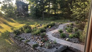 Un jardín ajardinado con un sendero curvo, un muro de piedra y una terraza de madera con escaleras que conducen a una casa.