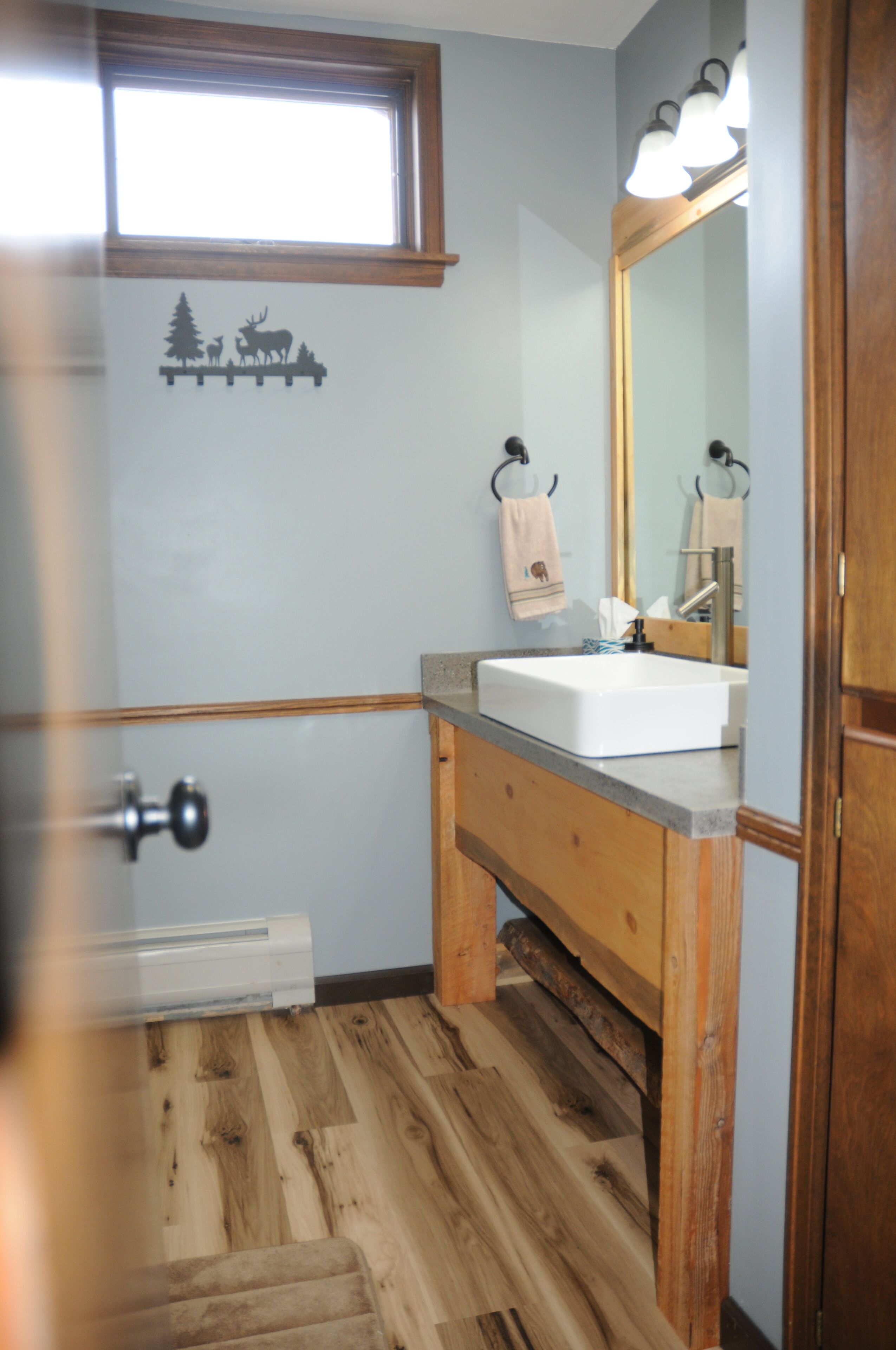 A bathroom with a wooden floor, a sink, a mirror, and a towel rack.