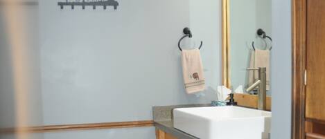 A bathroom with a wooden floor, a sink, a mirror, and a towel rack.