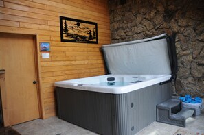 Ein Whirlpool mit Holzwand und Steinwand im Hintergrund, einer Holztür und einer kleinen Stufe, die zum Whirlpool führt.