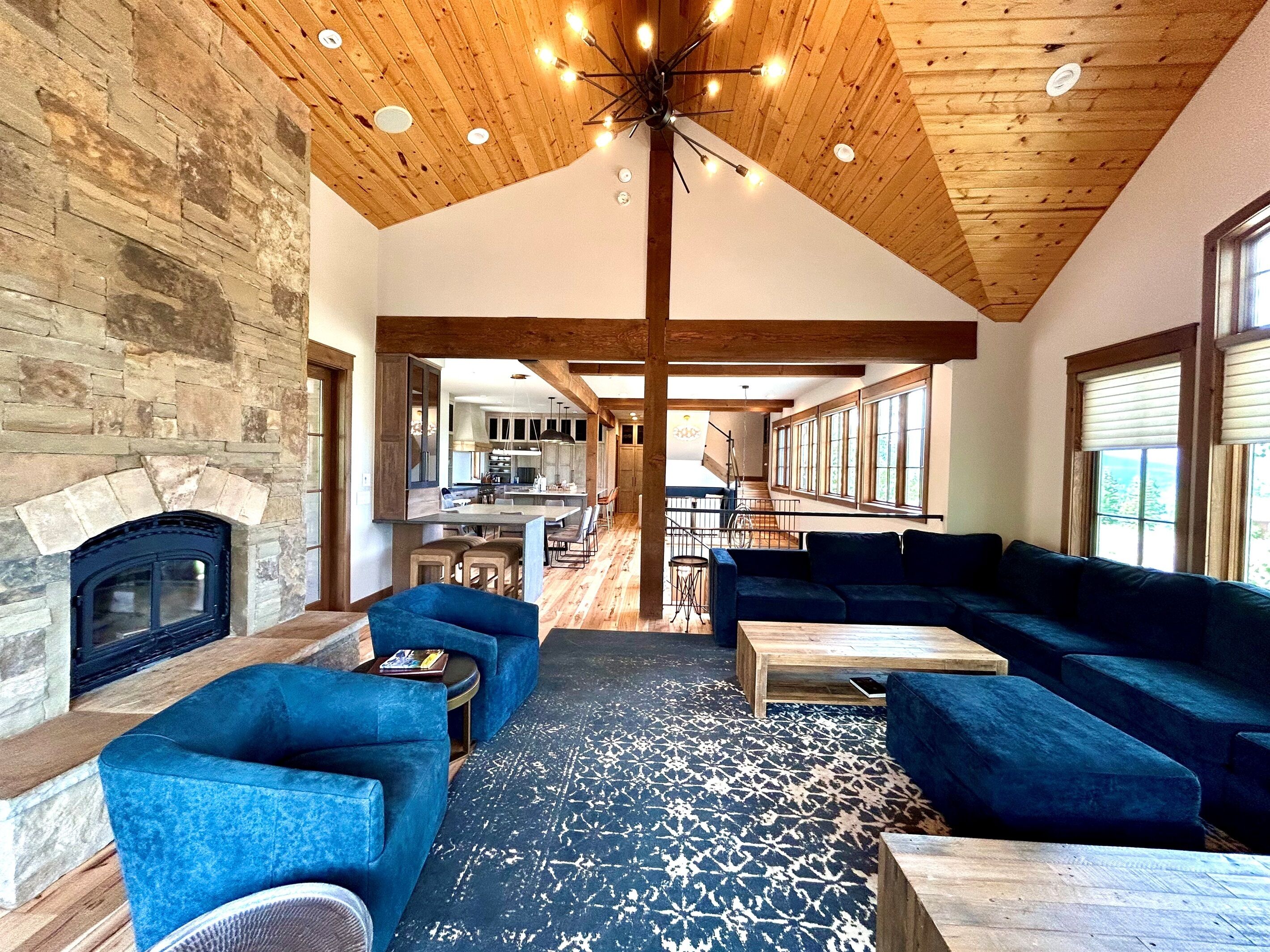 A spacious living area with a stone fireplace, blue sofas, and a wooden ceiling.