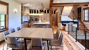 A spacious kitchen with a large island, wooden beams, and a dining area with chairs.