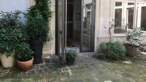 A building entrance with a glass door, potted plants, and a stone-paved courtyard. - Charming studio in the Marais (Paris)