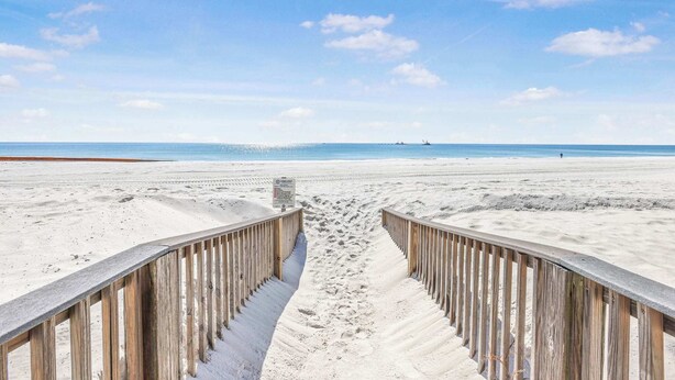Ein sandiger Strand mit einer hölzernen Promenade, die zum Wasser führt.