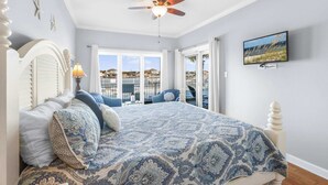 Ein Schlafzimmer mit einem großen Bett, einem Deckenventilator, einem Fernseher und Blick auf die Stadt durch die Fenster.