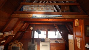 Una cocina rústica en el ático con vigas de madera, una estufa y una ventana con ollas colgando.